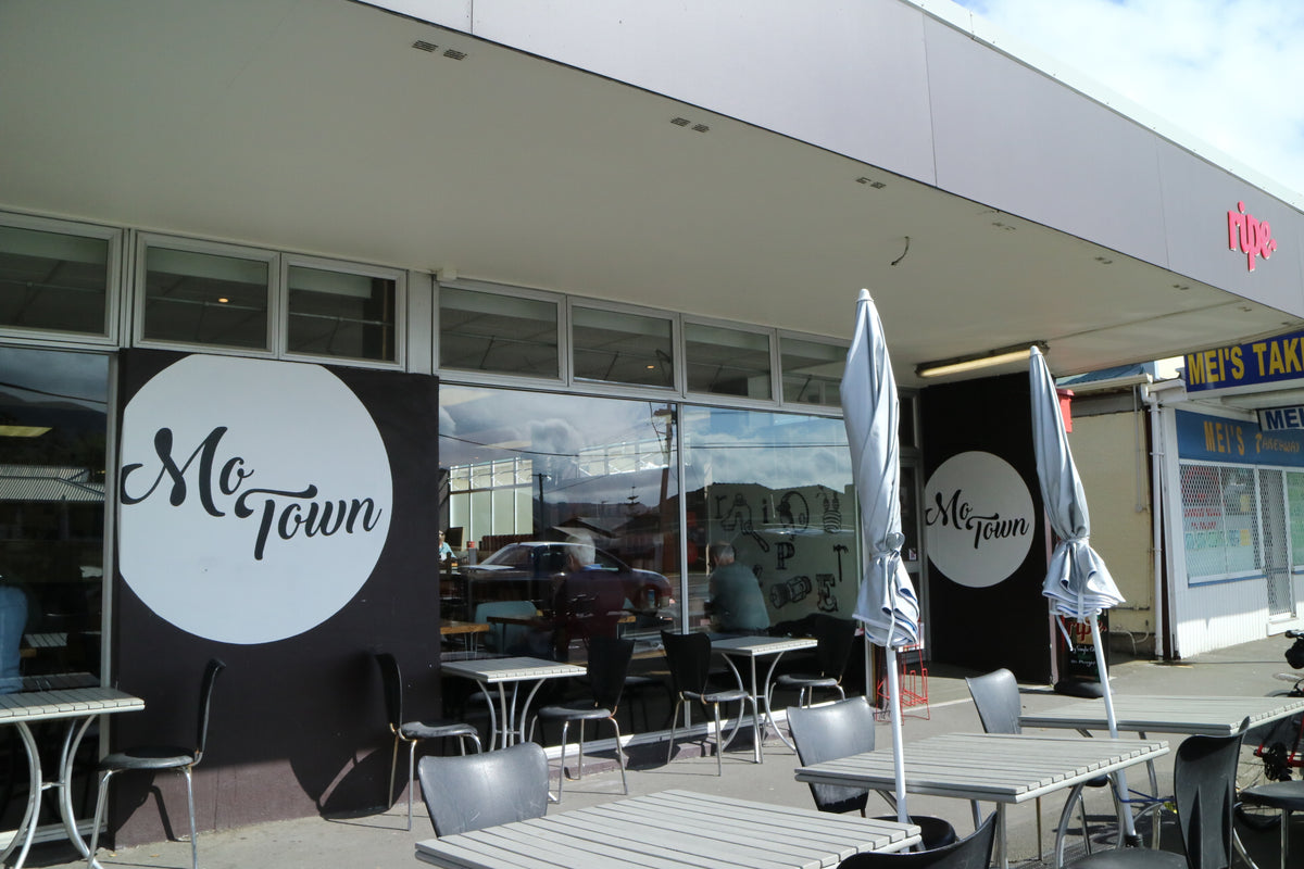 Outdoor seating area of MoTown cafe with black and white branded wall panels, closed patio umbrellas, and metal tables and chairs on a sidewalk.